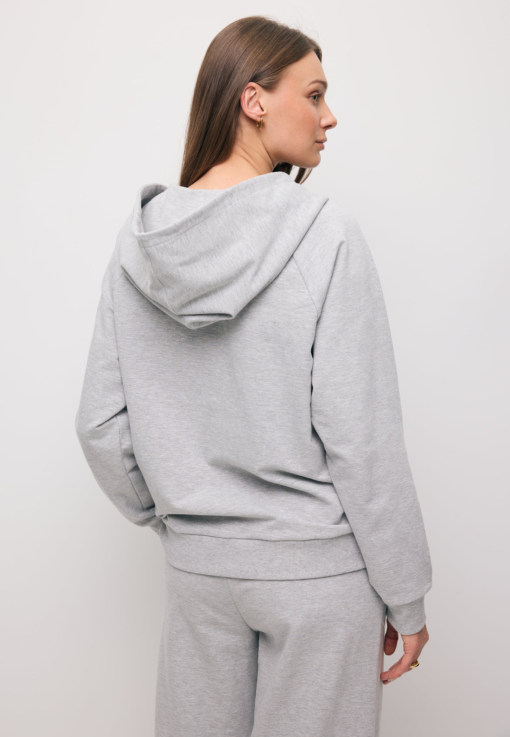 Zbliżenie na modelkę stojącą tyłem w szarej bluzie z kapturem IANELLA.