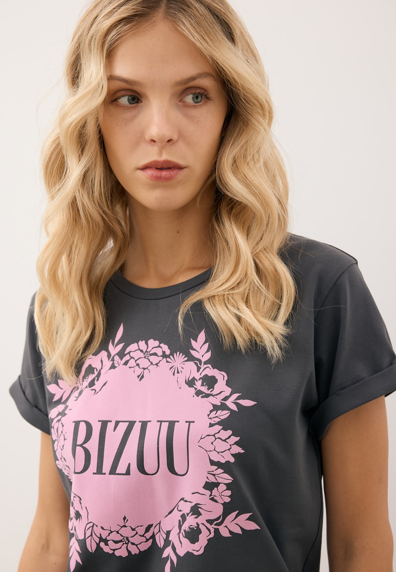 Zbliżenie na różową aplikację z logo Bizuu na grafitowym T-shircie IOLA.