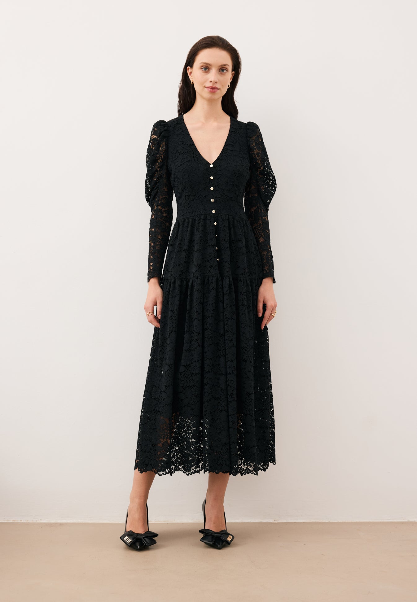 Modelka na tle białej ściany ubrana w midi sukienkę z koronki ISORELLA.