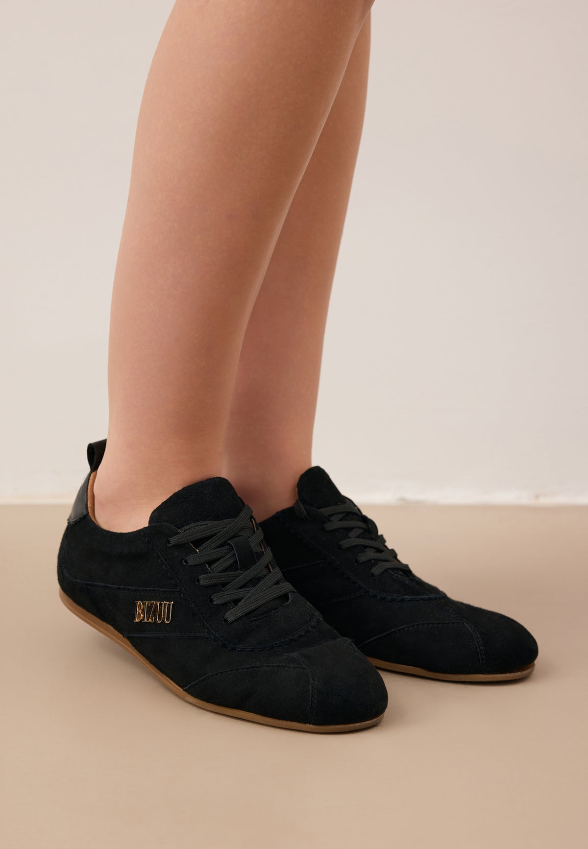 Zbliżenie na nogi modelki w czarnych zamszowych sneakersach LEOLA ze złotym logo z boku.