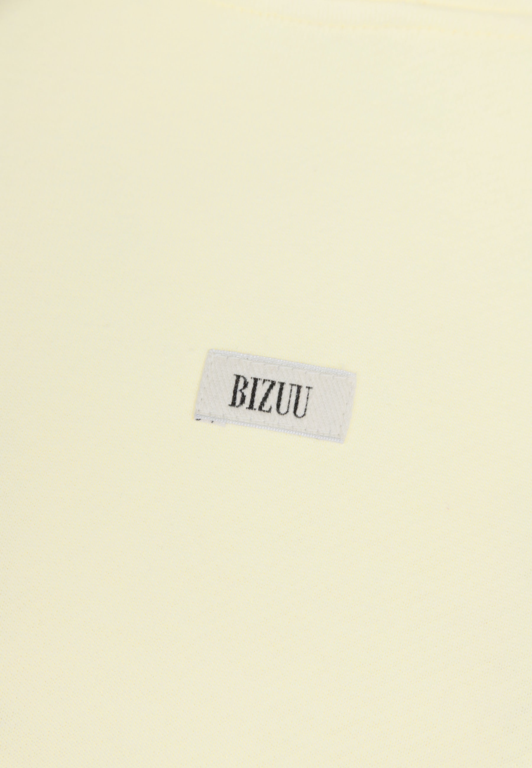 Zbliżenie na metkę z logo Bizuu umieszczoną na przodzie żółtej bluzy LINDA.