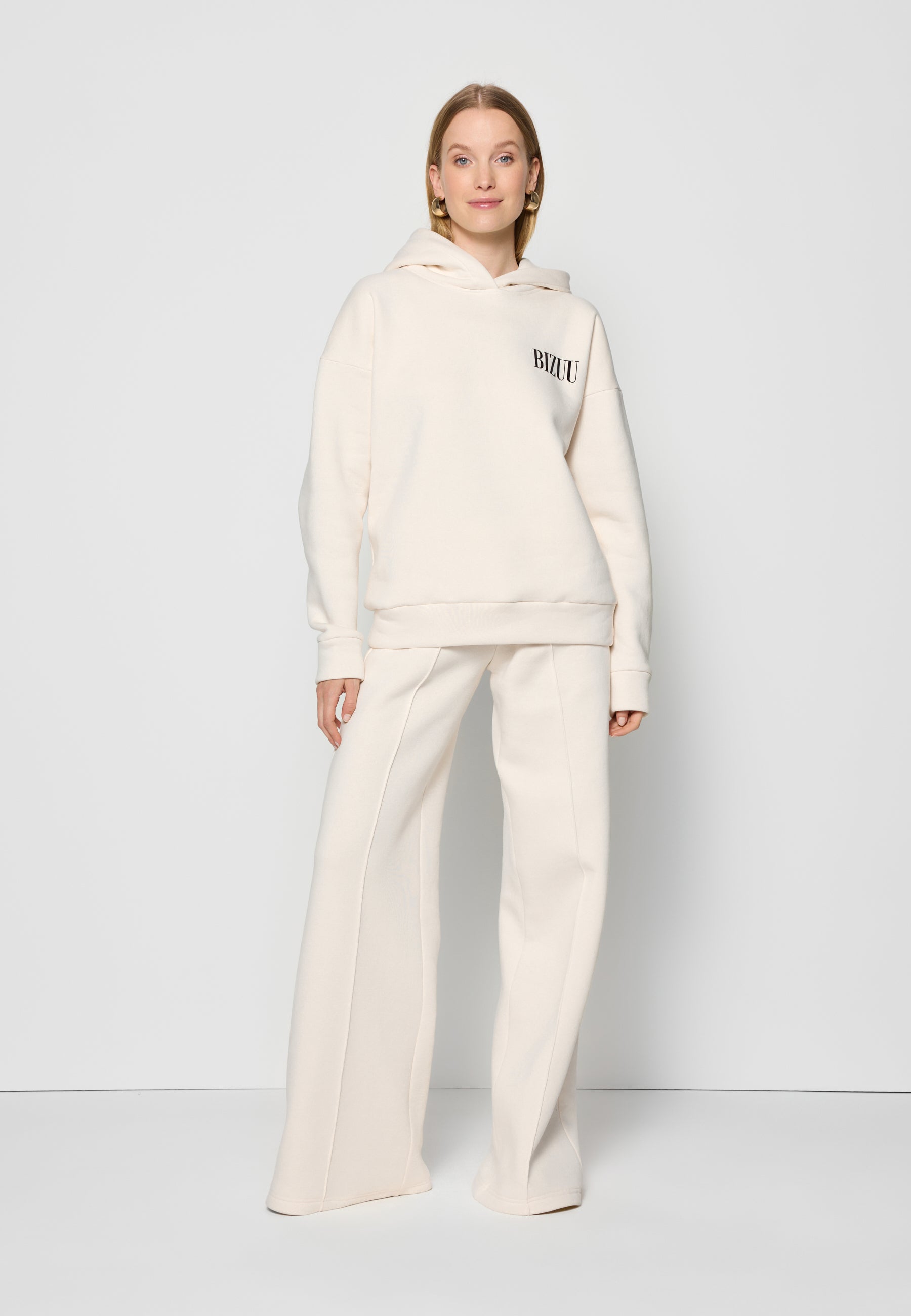 Modelka na białym tle ubrana w kremowy zestaw dresowy LINDI i PETRA.