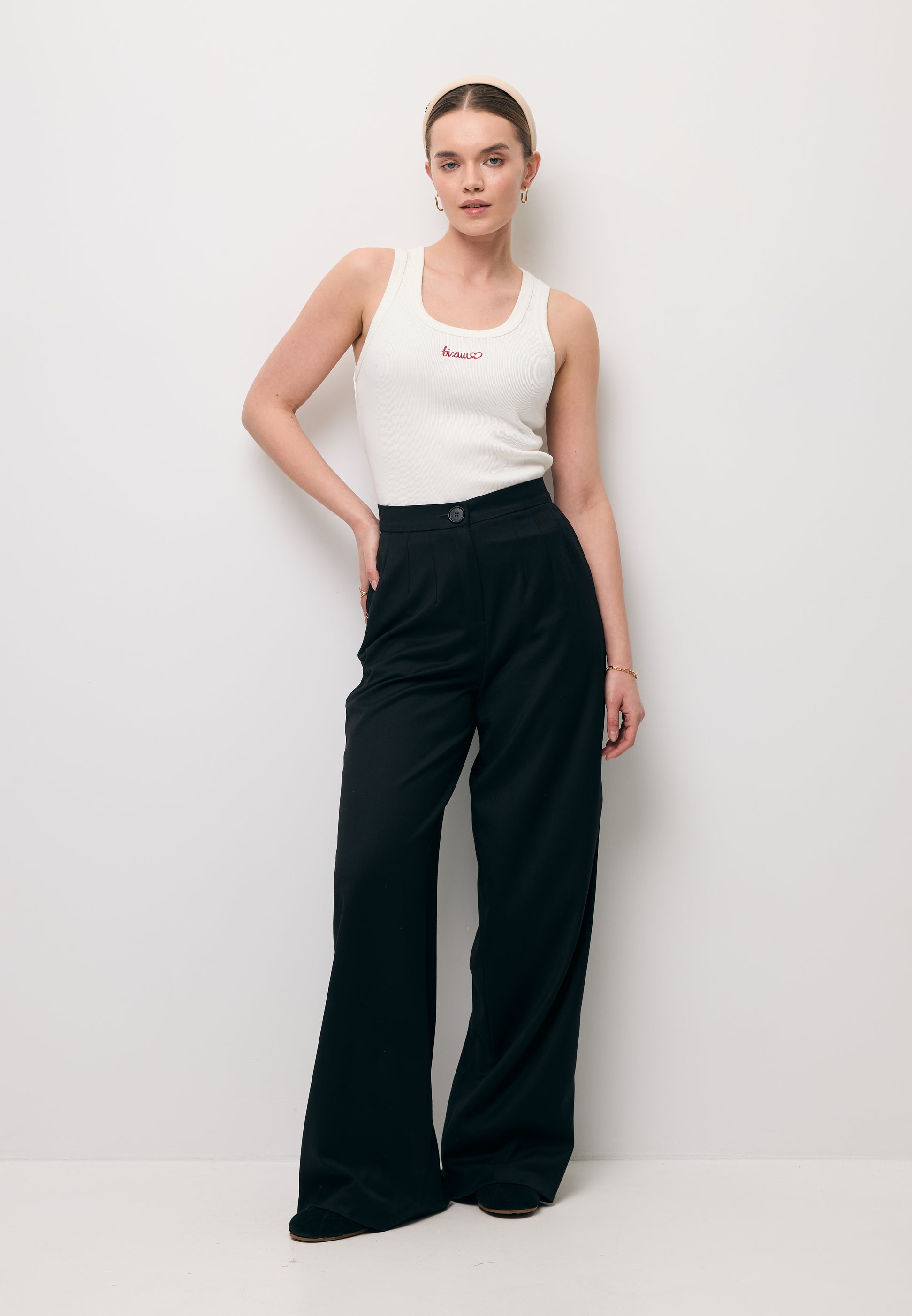 Pełna postać modelki ubrana w biały top LOVIE z haftem na przodzie oraz czarnych spodniach MICHAEL.