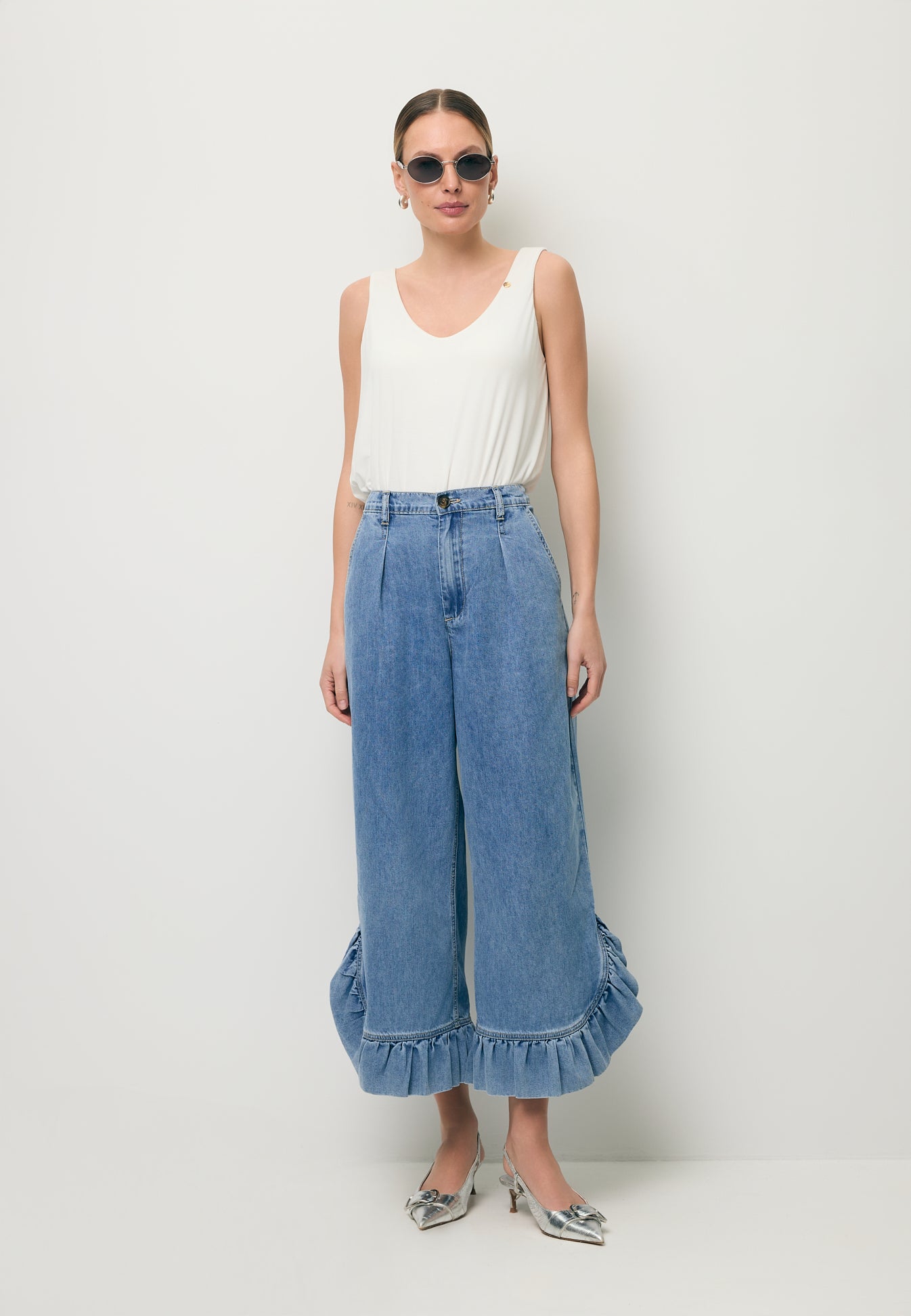 Modelka ubrana w kremowy top LULY oraz jeansowe spodnie NELLA z ozdobną falbaną na nogawce.