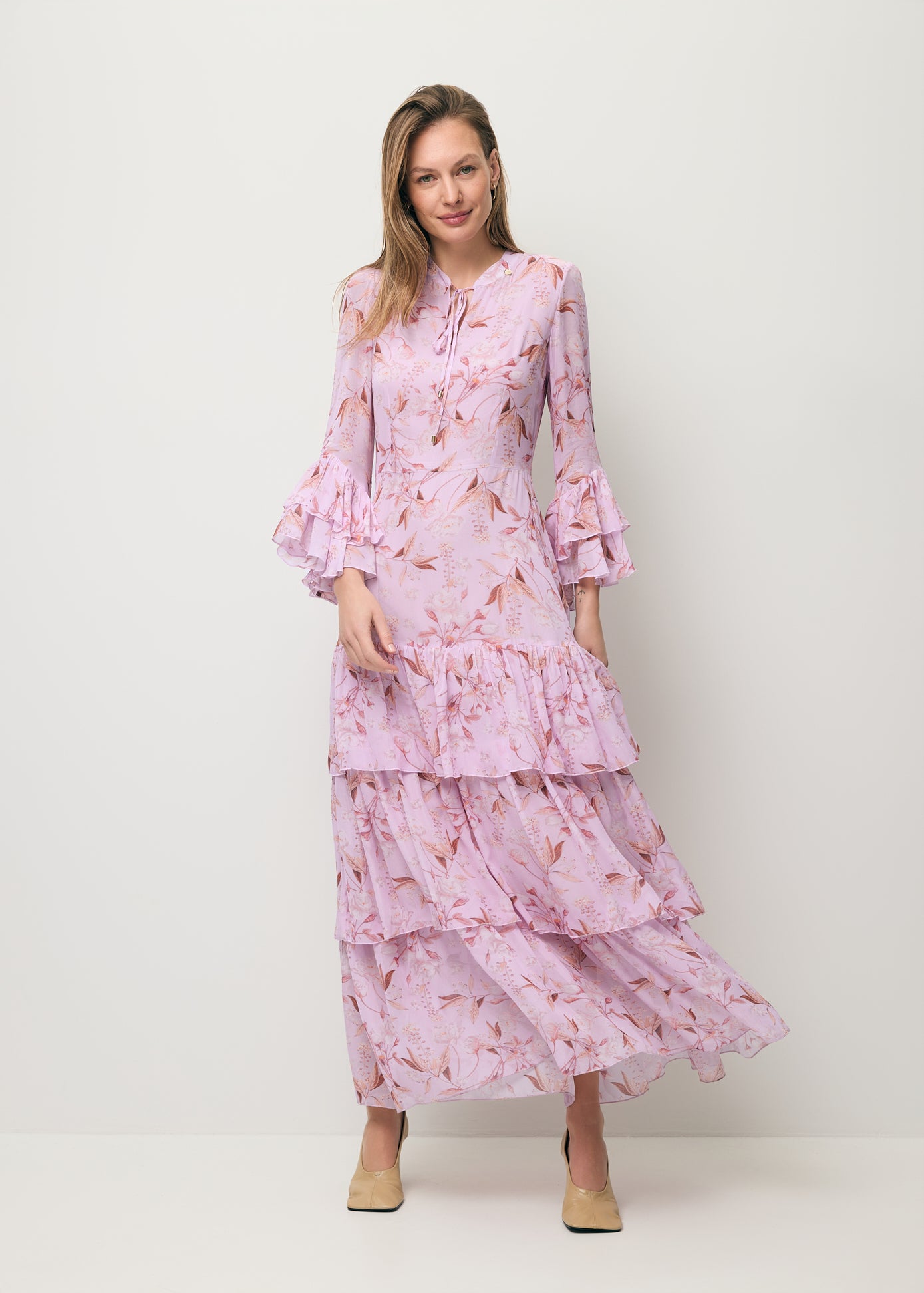 Modelka ubrana w zwiewną sukienkę z ozdobnymi falbanami MASSI w kolorze różowym.