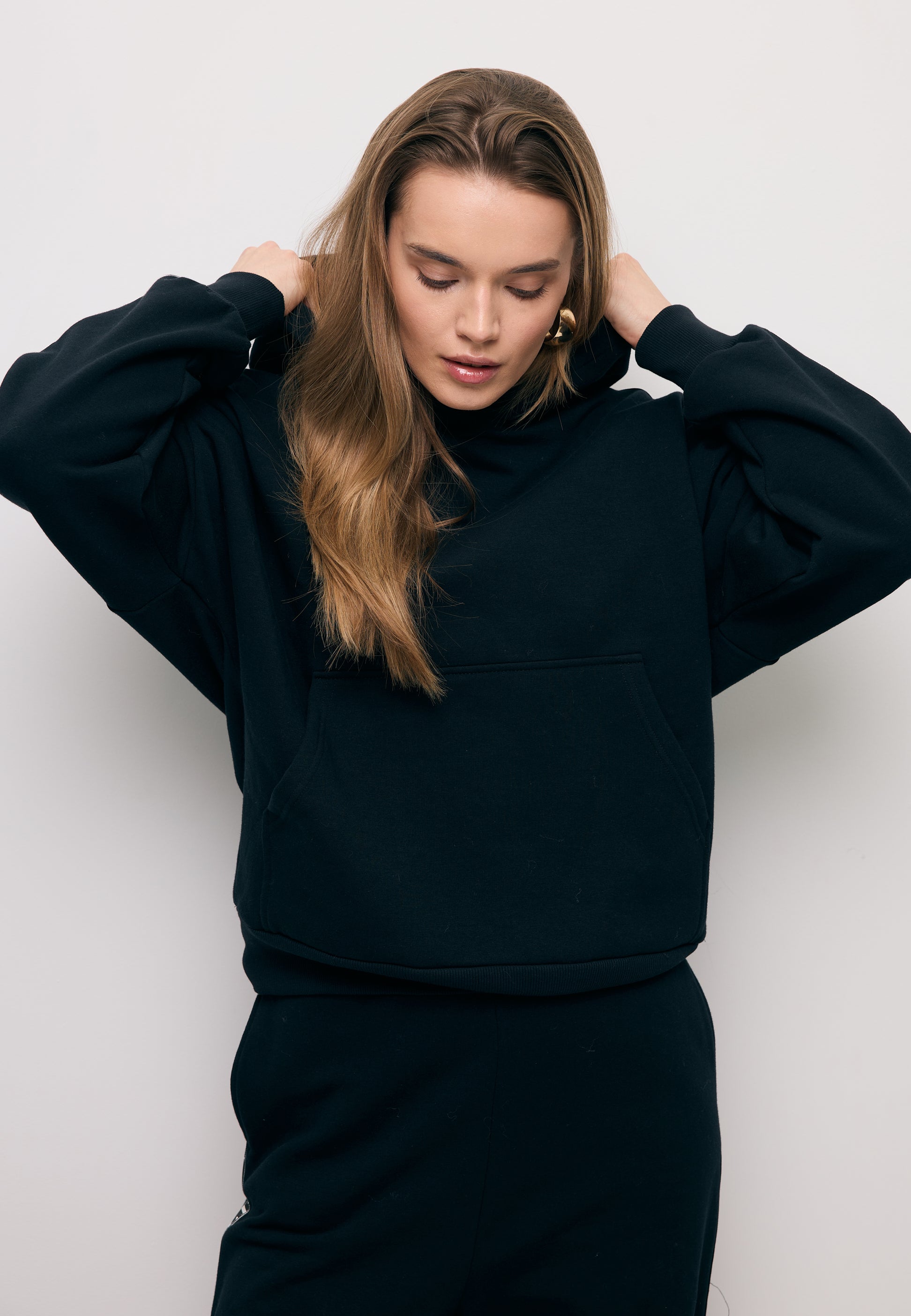 Zbliżenie na modelkę poprawiającą kaptur w czarnej bluzie z lampasem na rękawie MAYRA.