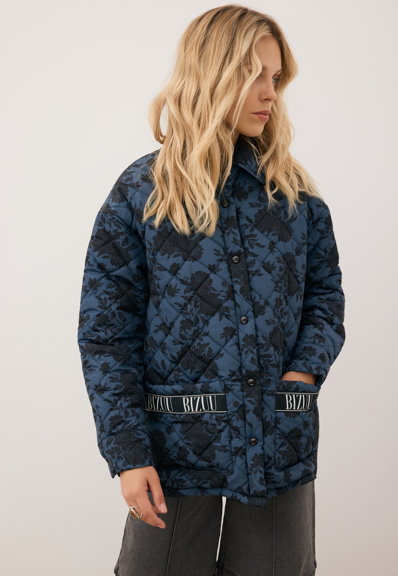 Zbliżenie na kurtkę pikowaną w print MARIN na modelce stojącej na tle białej ściany.