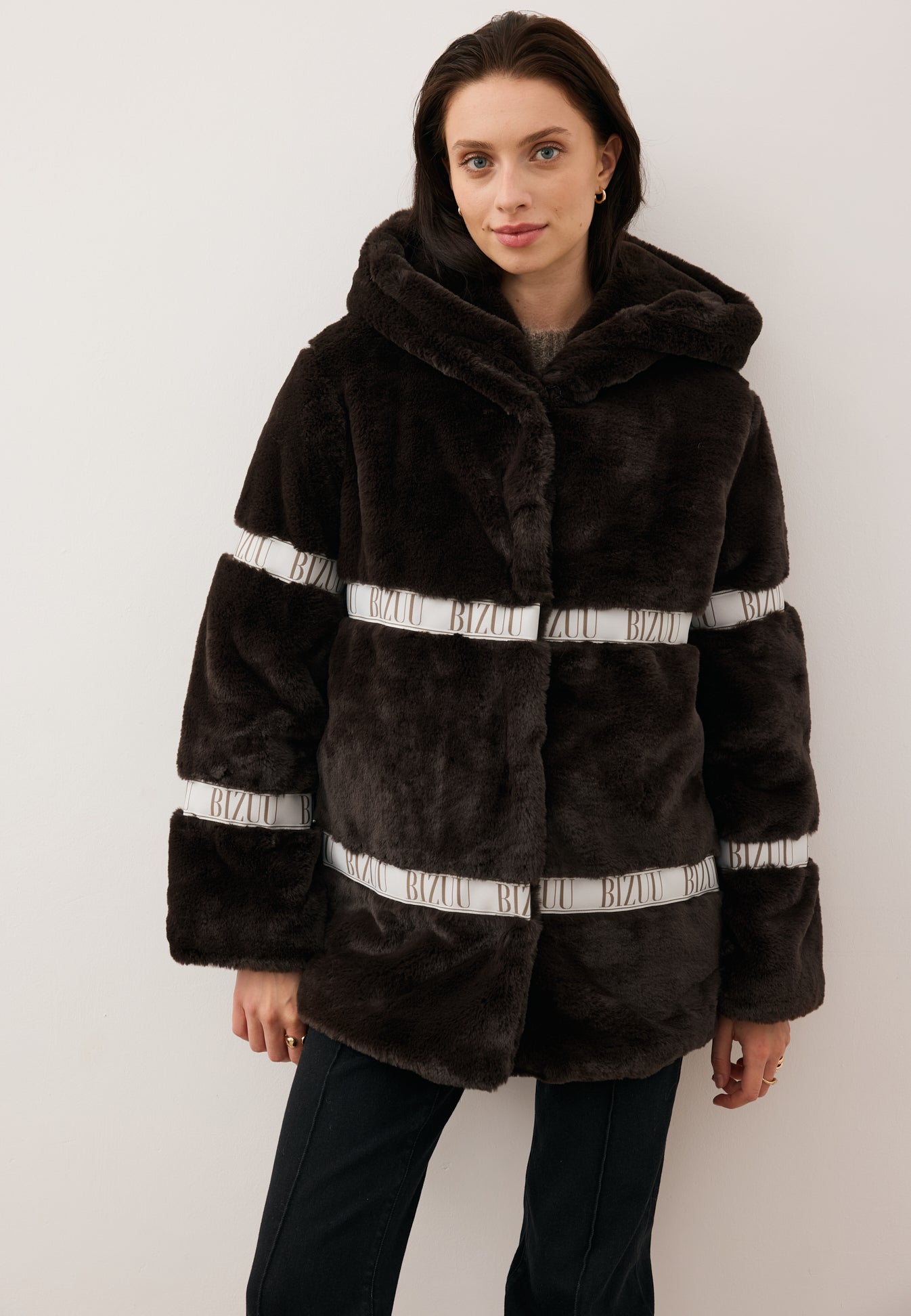 Modelka stojąca przodem w brązowym futerku z logowaniem i kapturem MILANO.