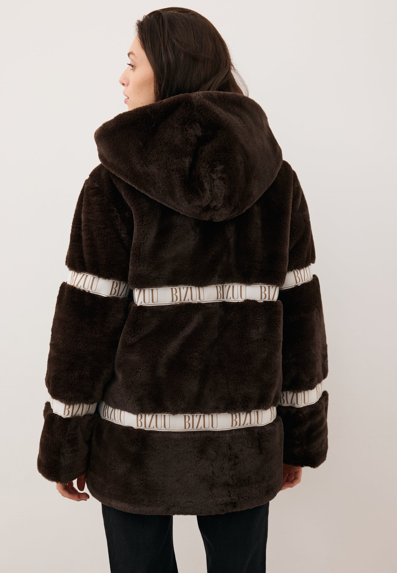 Modelka stojąca tyłem w futerku z kapturem MILANO w kolorze brązowym.