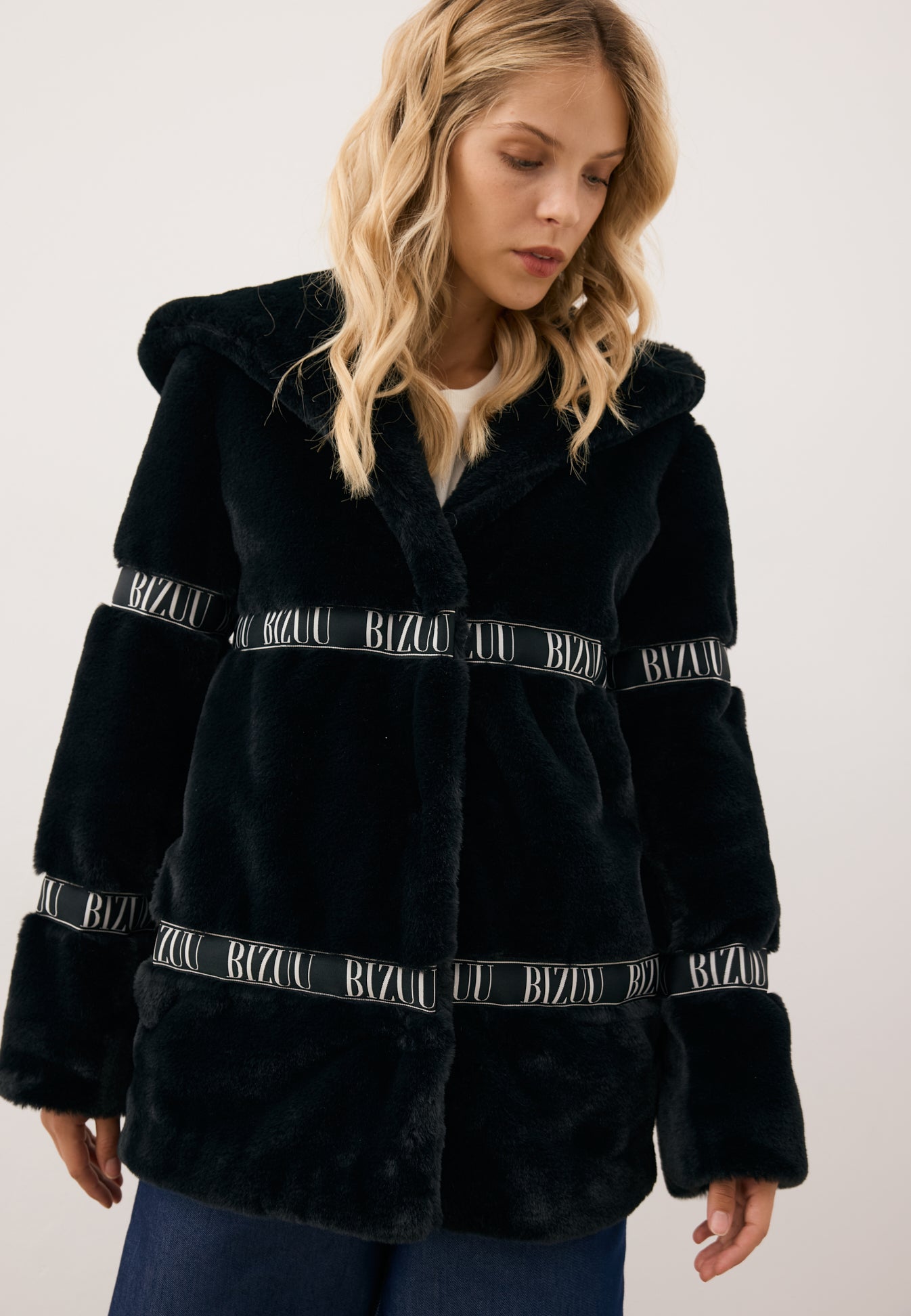 Modelka patrząca w bok ubrana w czarne logowane futerko z kapturem MIALNO.