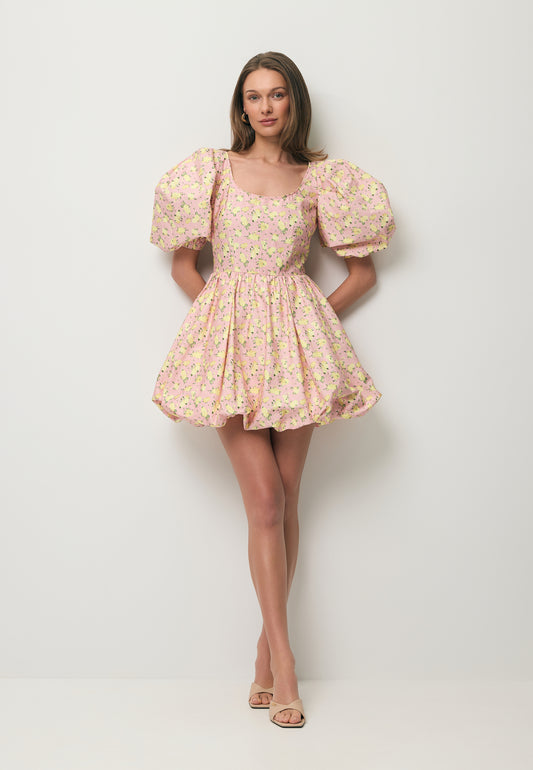 Modelka na tle białej ściany ubrana w sukienkę MOSY w kwiatowy print i balonowy dół.