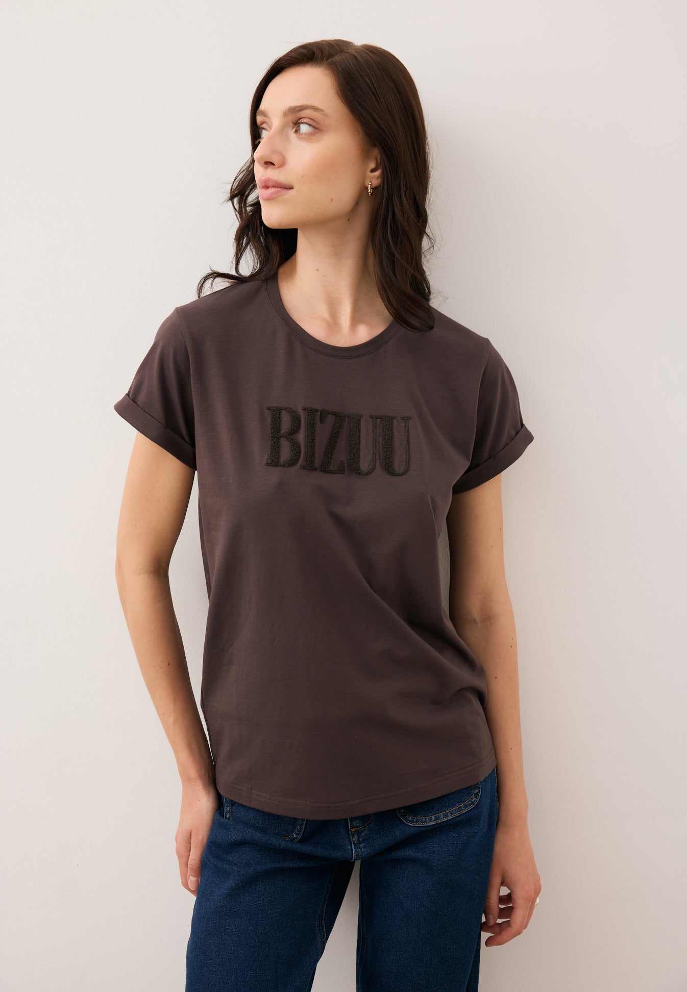 Modelka patrząca w bok w brązowym T-shircie z logo na przodzie NIKKO.