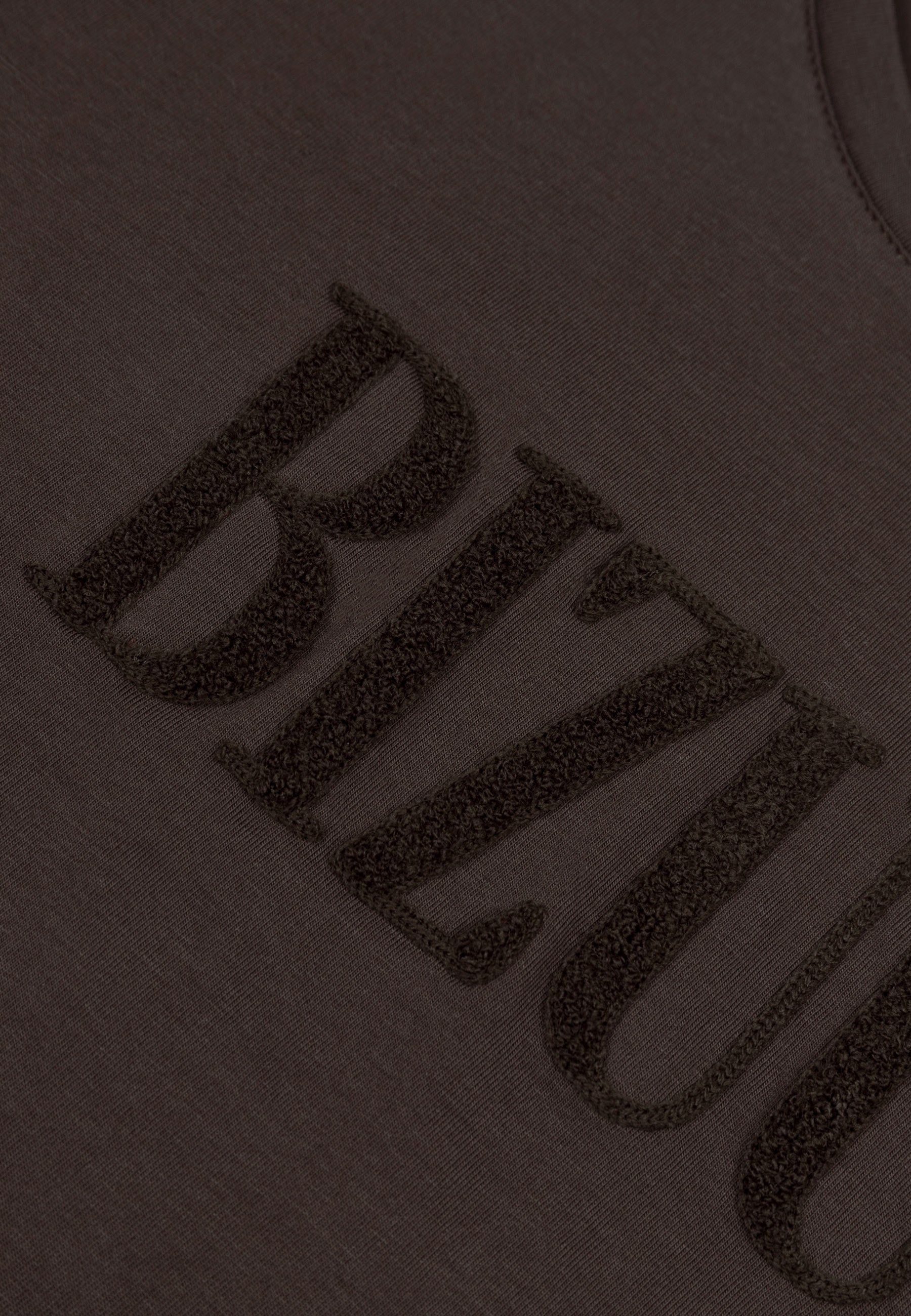Zbliżenie na wypukłe logo na brązowym T-shircie NIKKO.