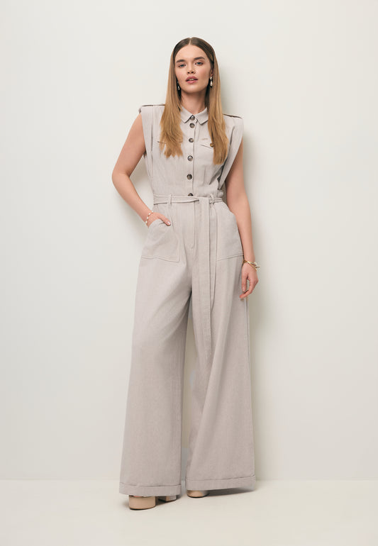 Modelka na tle białej ściany ubrana w beżowy kombinezon NINGINO z szerokimi nogawkami i wiązaniem w talii.