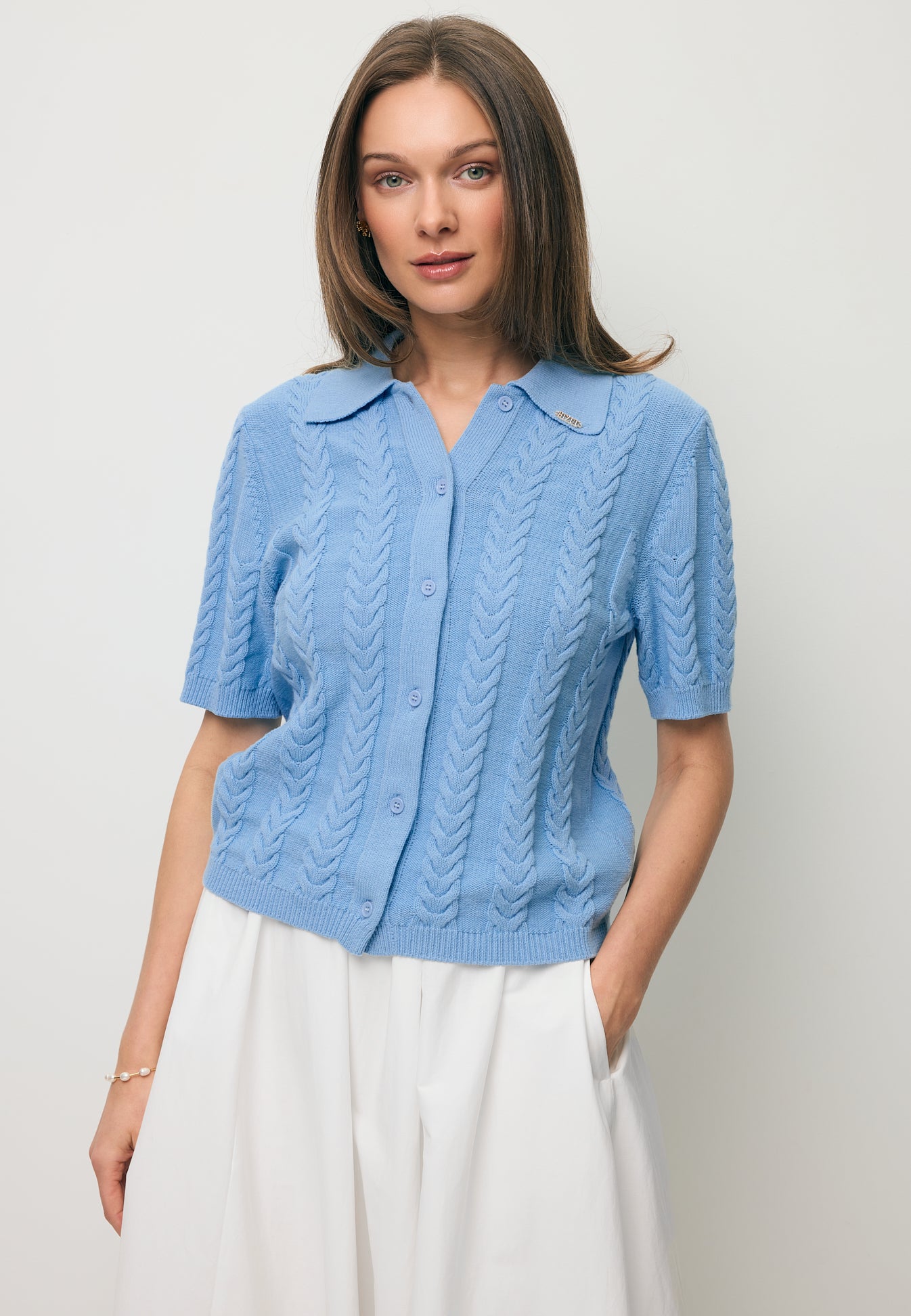 Zbliżenie na modelkę trzymającą rękę w kieszeni kremowej spódnicy NUBE, ubrana w niebieski sweterek z kołnierzykiem i krótkim rękawem PATRI.