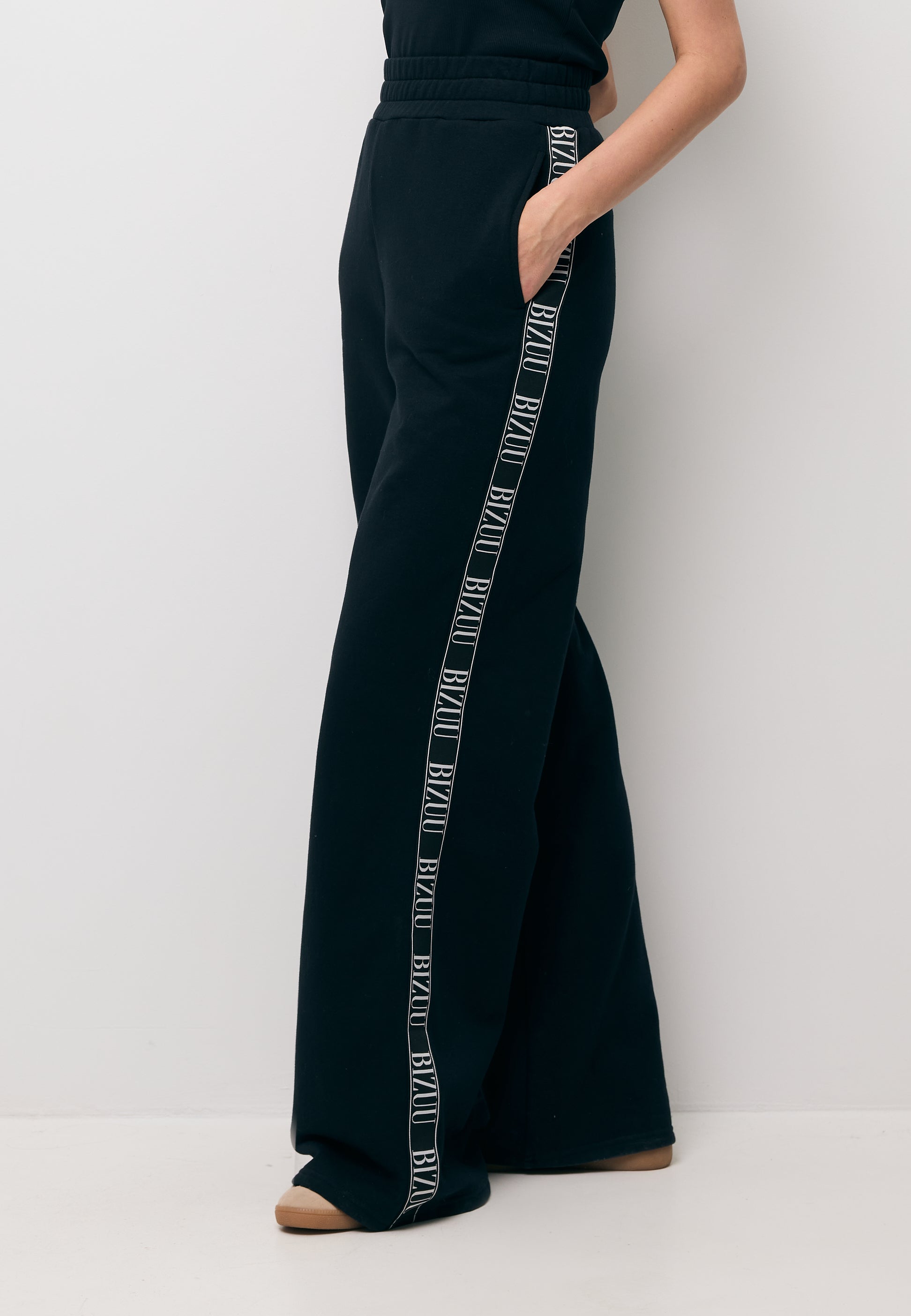 Zbliżenie na nogi modelki w czarnych spodniach dresowych o szerokiej nogawce PETRY.