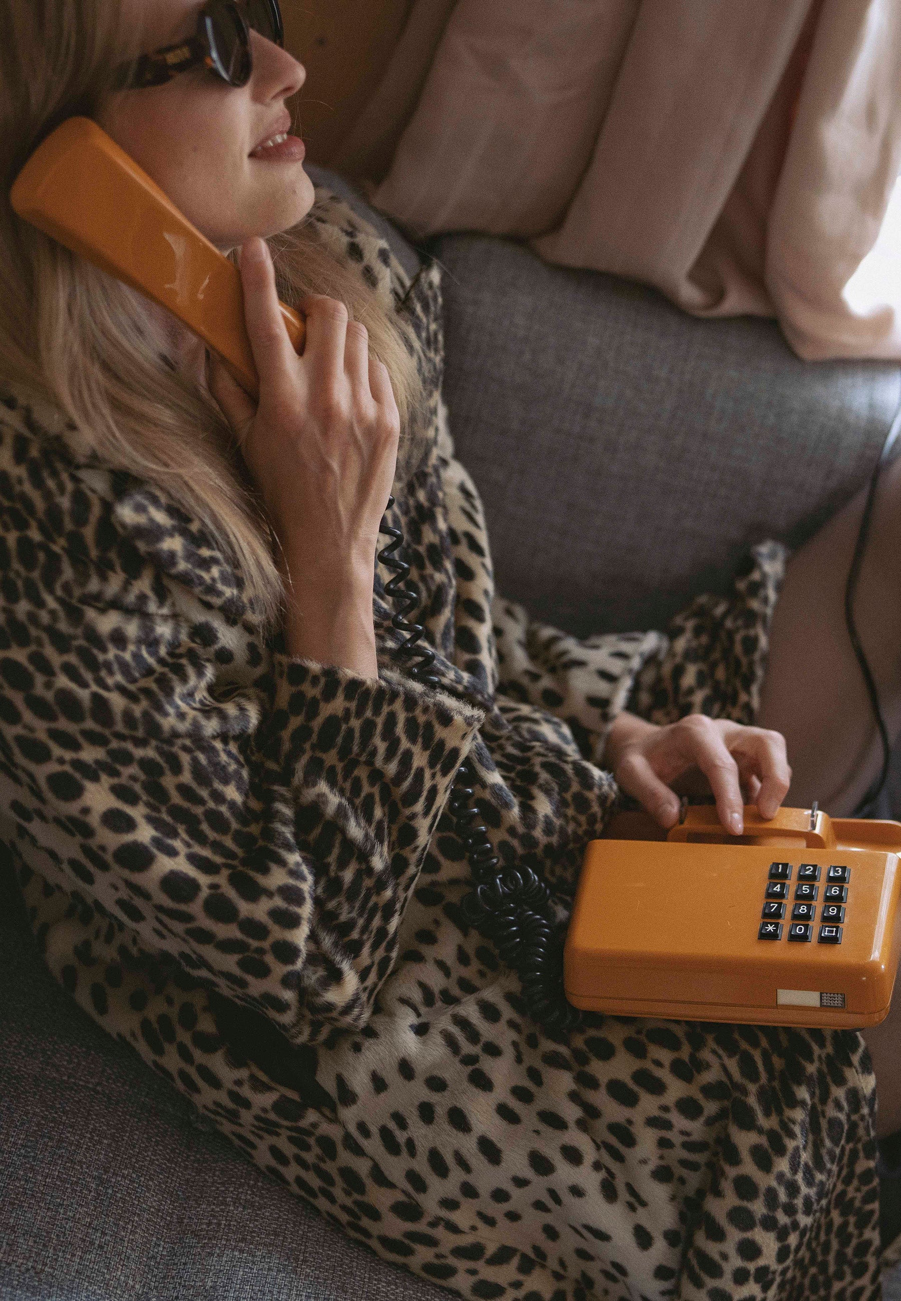 Modelka siedząca na kanapie, rozmawiająca przez telefon stacjonarny ubrana w płaszcz w panterkę POTICELLI z tłoczoną metką z logo na rękawie.