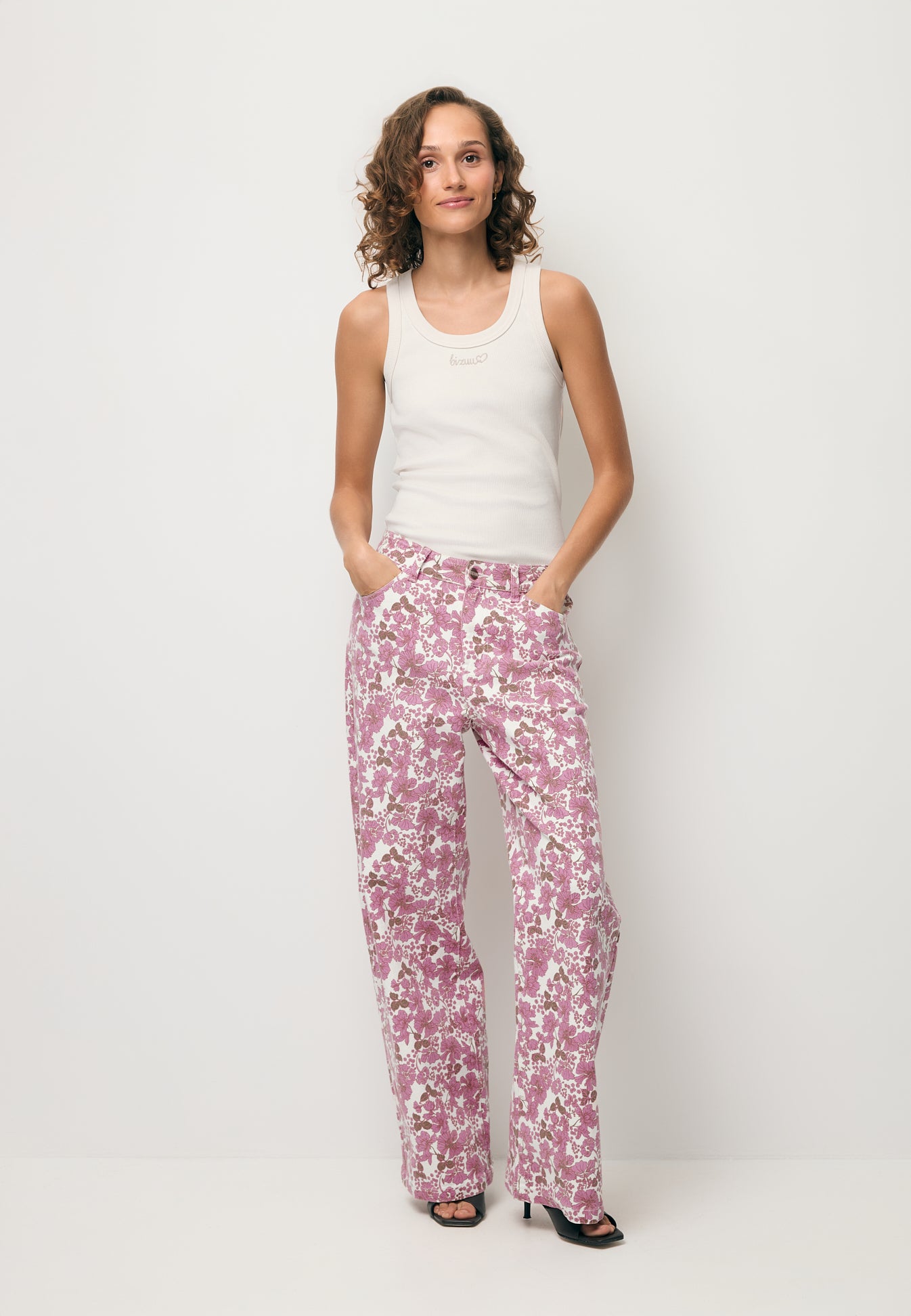 Modelka trzymająca ręce w kieszeni jeansów w kwiatowy print DONY, ubrana w biały top z beżowym logo LOVIE.