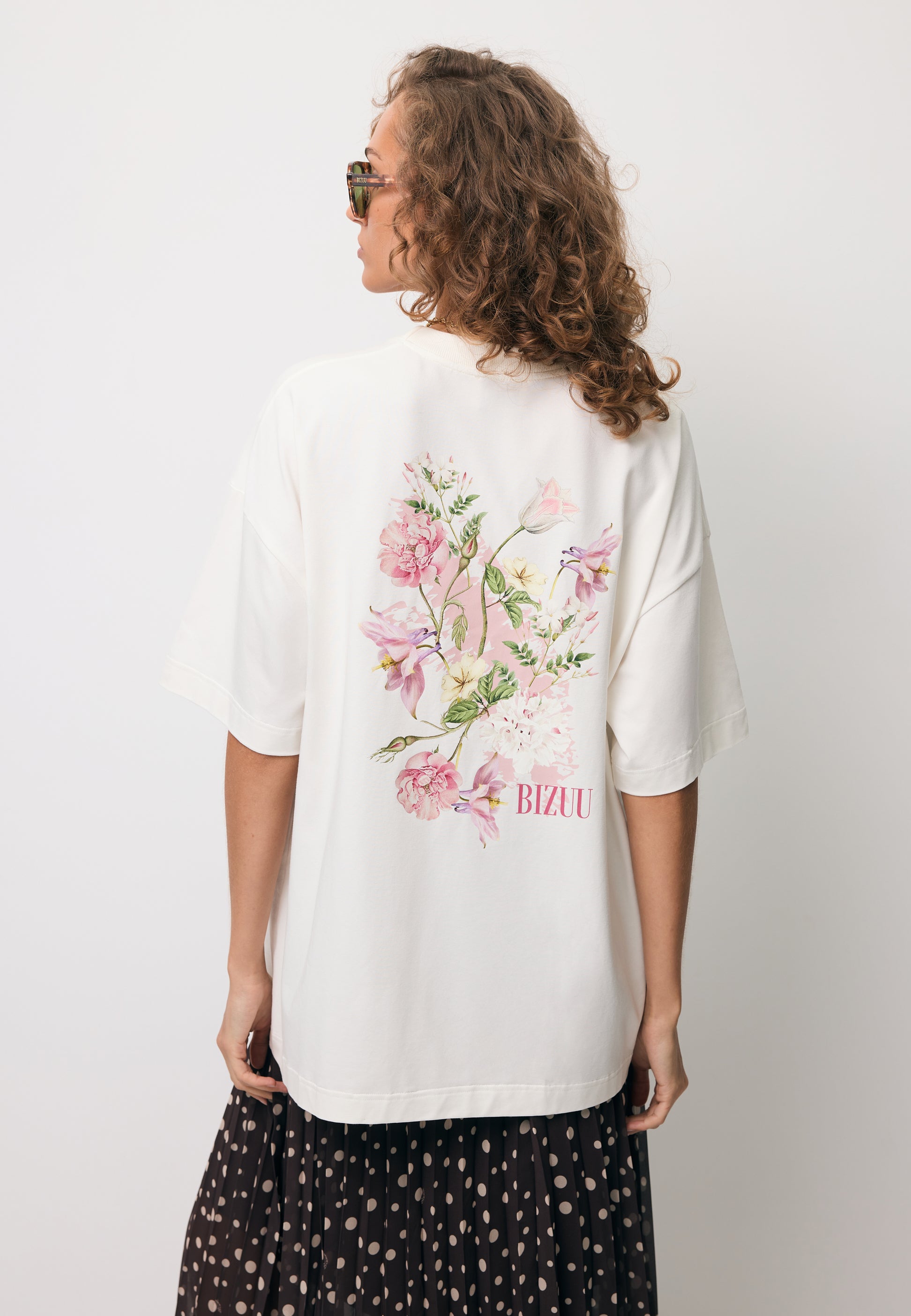 Zbliżenie na modelkę stojącą tyłem w T-shircie RIONA z nadrukiem na tyle.