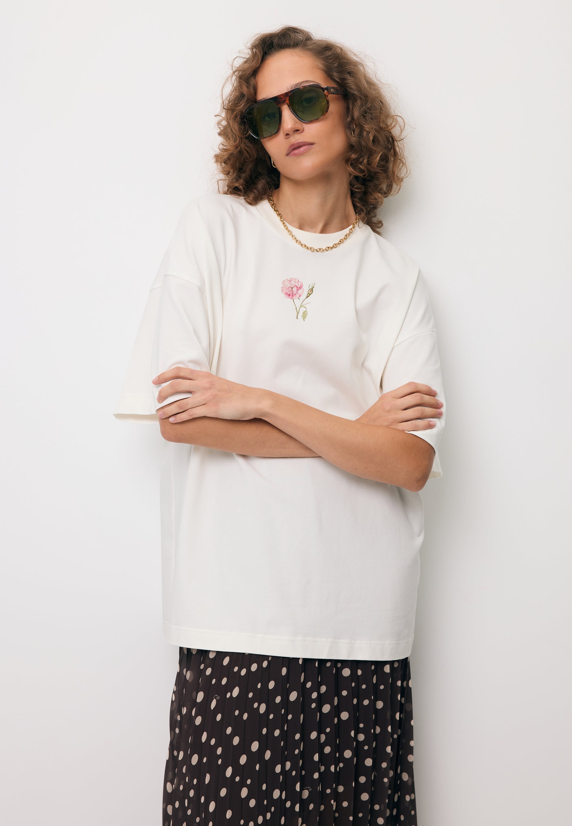 Zbliżenie na modelkę opartą o ścianę ubraną w oversizowy T-shirt RIONA w kolorze kremowym.