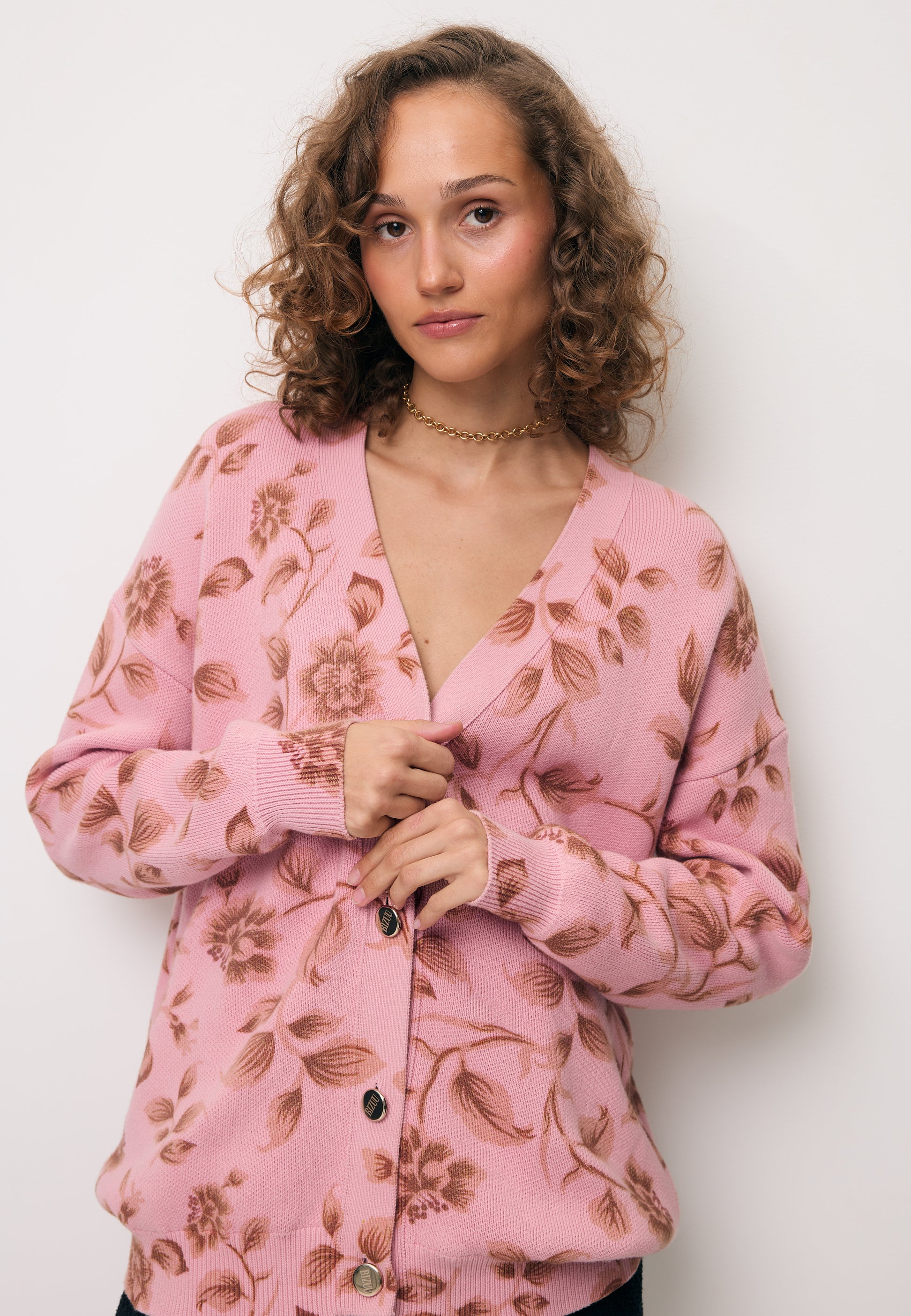 Zbliżenie na modelkę w różowym swetrze zapinanym na złote guziki ROSSY.
