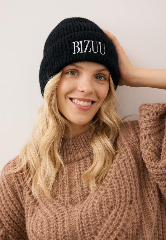 Zbliżenie na uśmiechniętą modelkę w czarnej czapce z wełną merino i białym, haftowanym logo ROYU