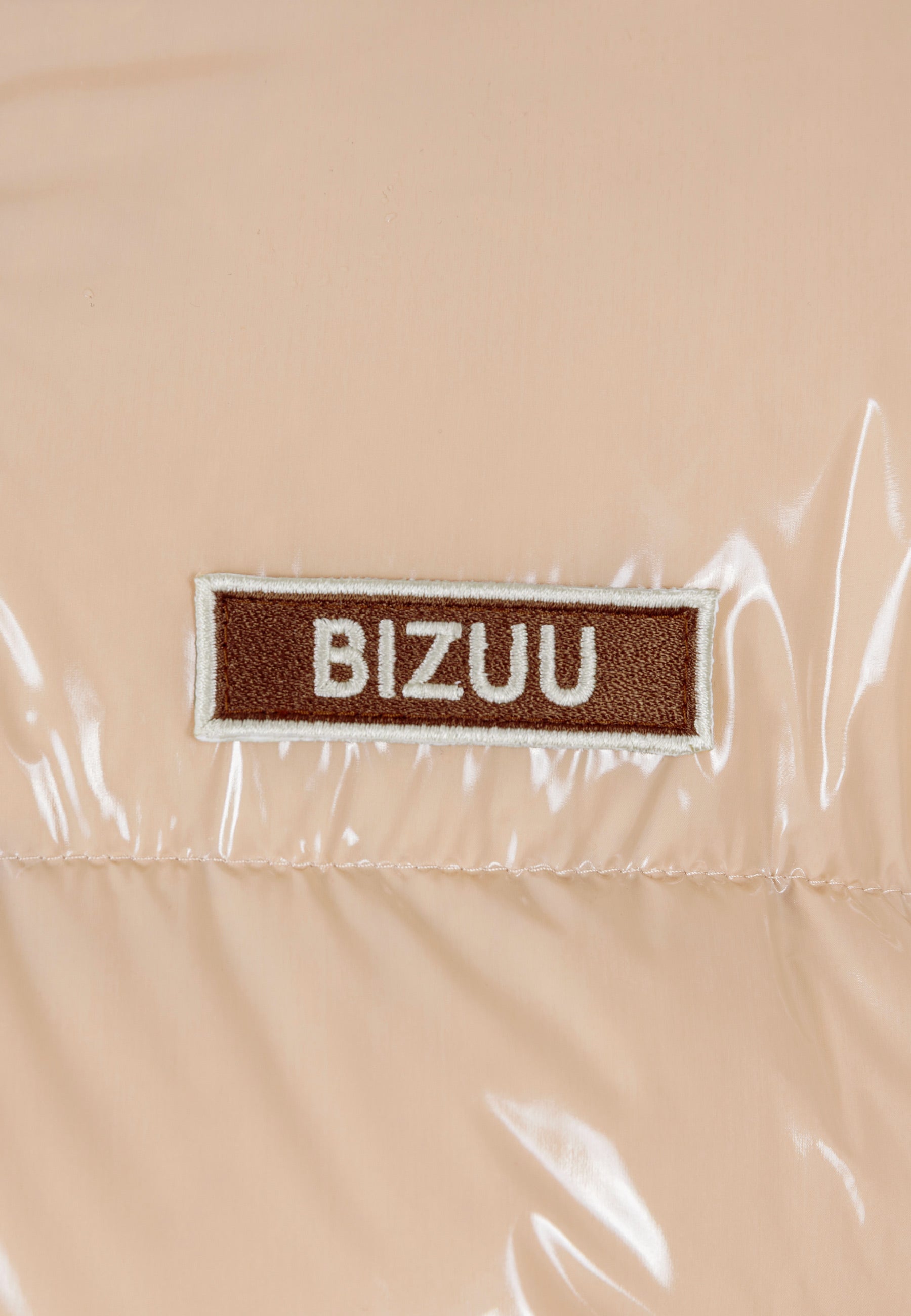 Zbliżenie na logo na beżowej kurtce SANYA.