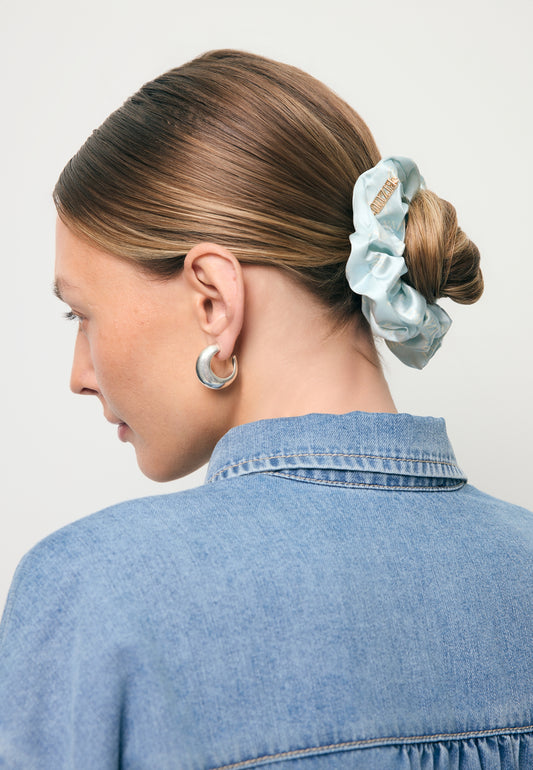Zbliżenie na włosy modelki upięte w kok ozdobiony jedwabną gumką w logo SILKY w kolorze niebieskim.