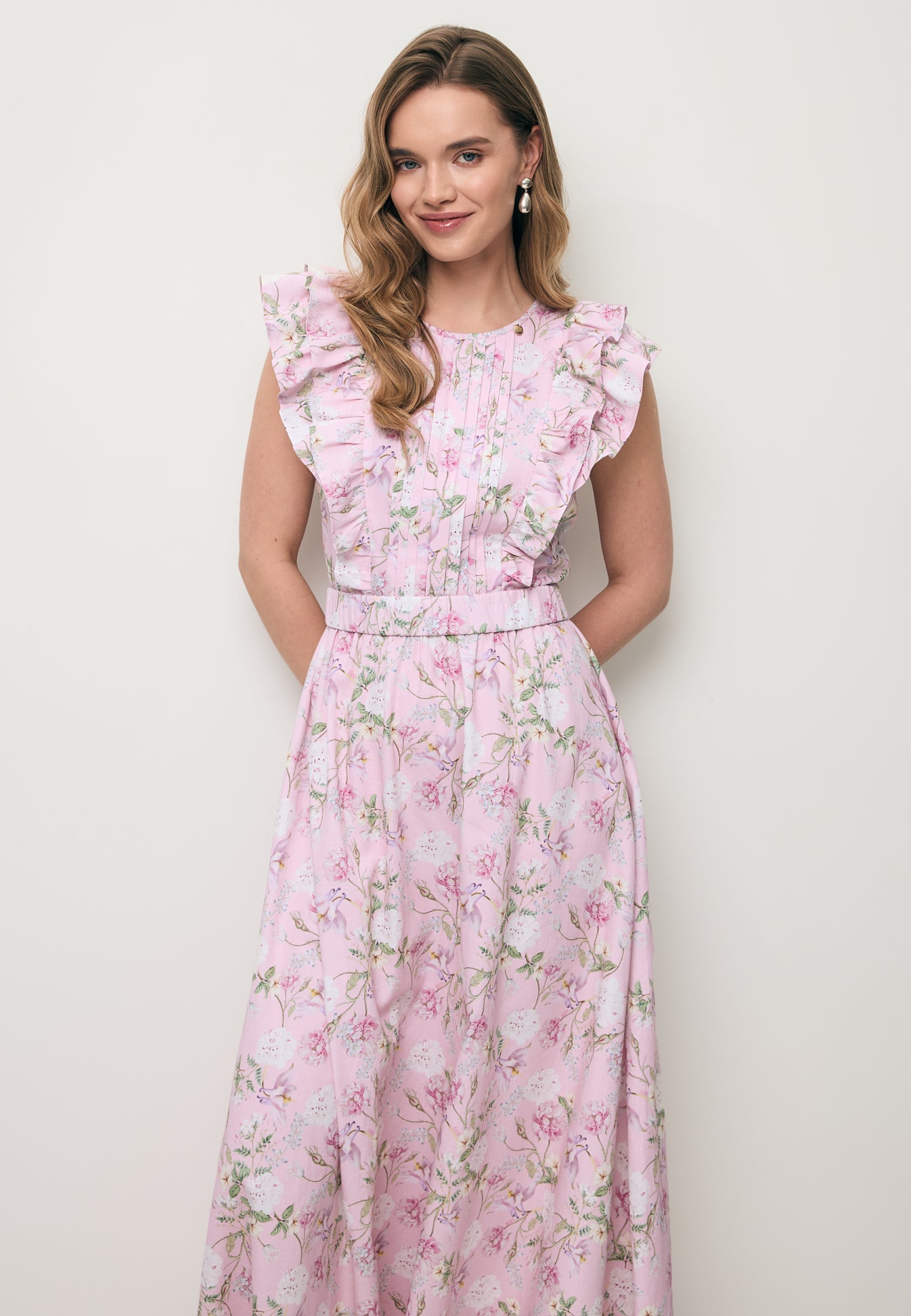 Uśmiechnięta modelka ubrana w kwiatową sukienkę midi SOLJA w kolorze różowym.