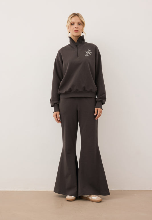 Modelka ubrana w czekoladowy dres z bluzą half zip TANSY i spodniami z szerokimi nogawkami ZEIA.