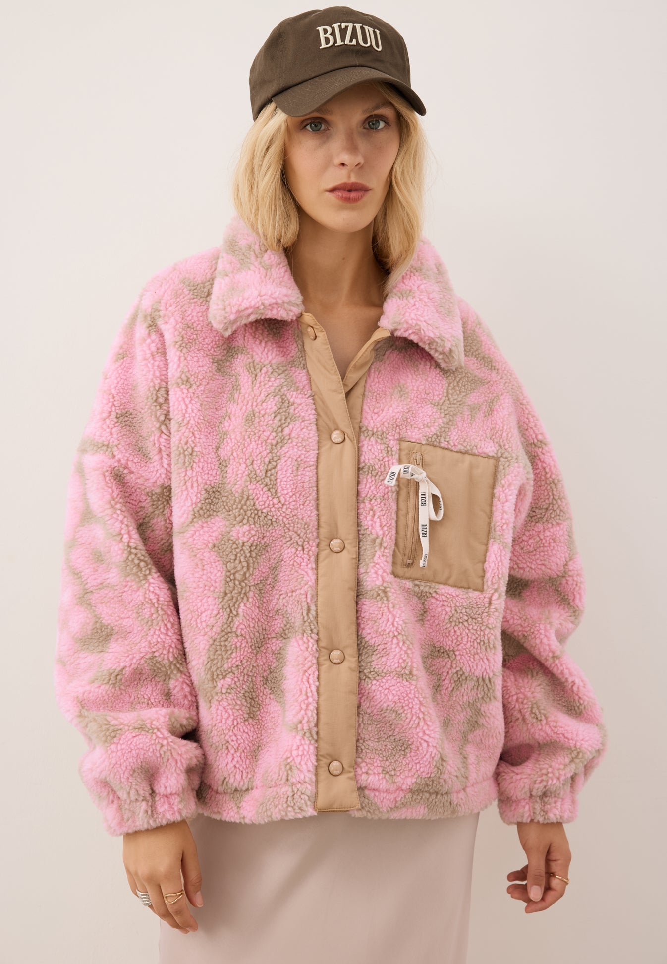 Modelka ubrana w polarową kurtkę TEDDY w kwiatowy wzór w kolorach różowo-beżowych. Na głowie ma założoną brązową czapkę z daszkiem ZANE.