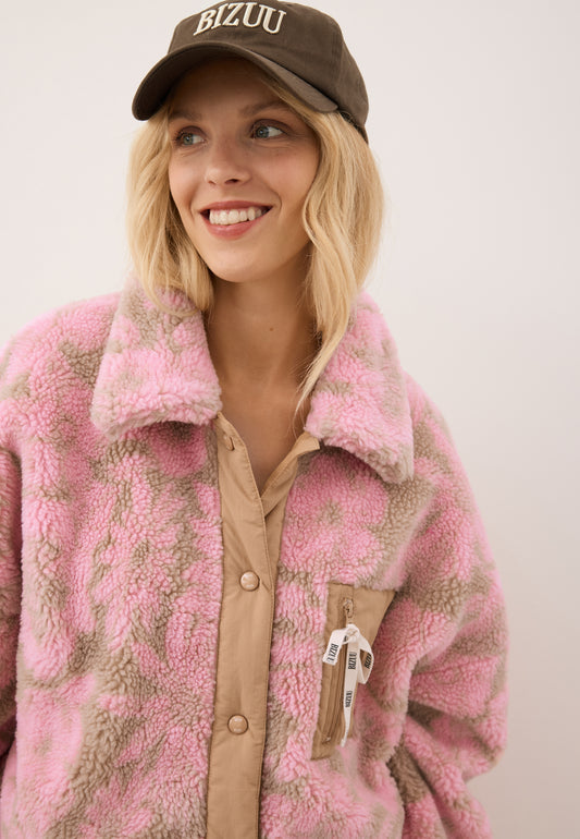 Zbliżenie na uśmiechniętą modelkę ubraną w kurtę z polaru TEDDY w kwiatowy wzór z ozdobną, logowaną kokardką oraz brązową czapkę z daszkiem ZANE.