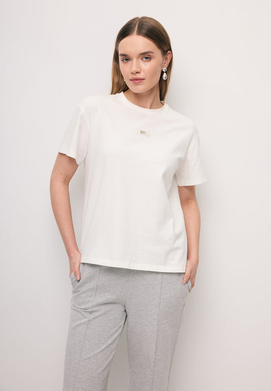 Zbliżenie na modelkę ubraną w biały t-shirt TISHAL ze złotym logo na przodzie.