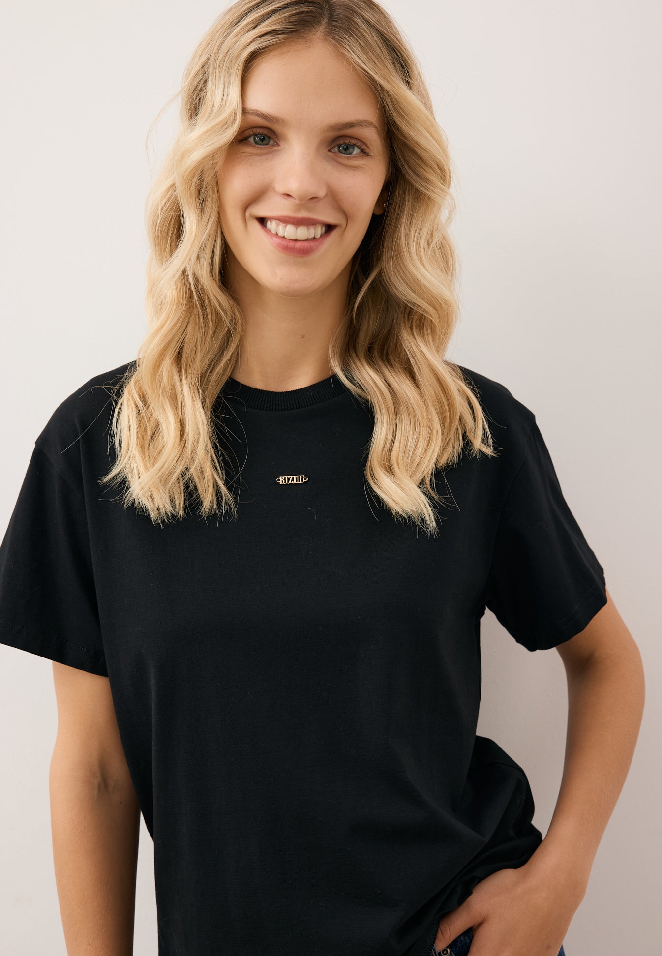 Zbliżenie na modelkę w czarnym T-shircie TISHAL z logo na przodzie.