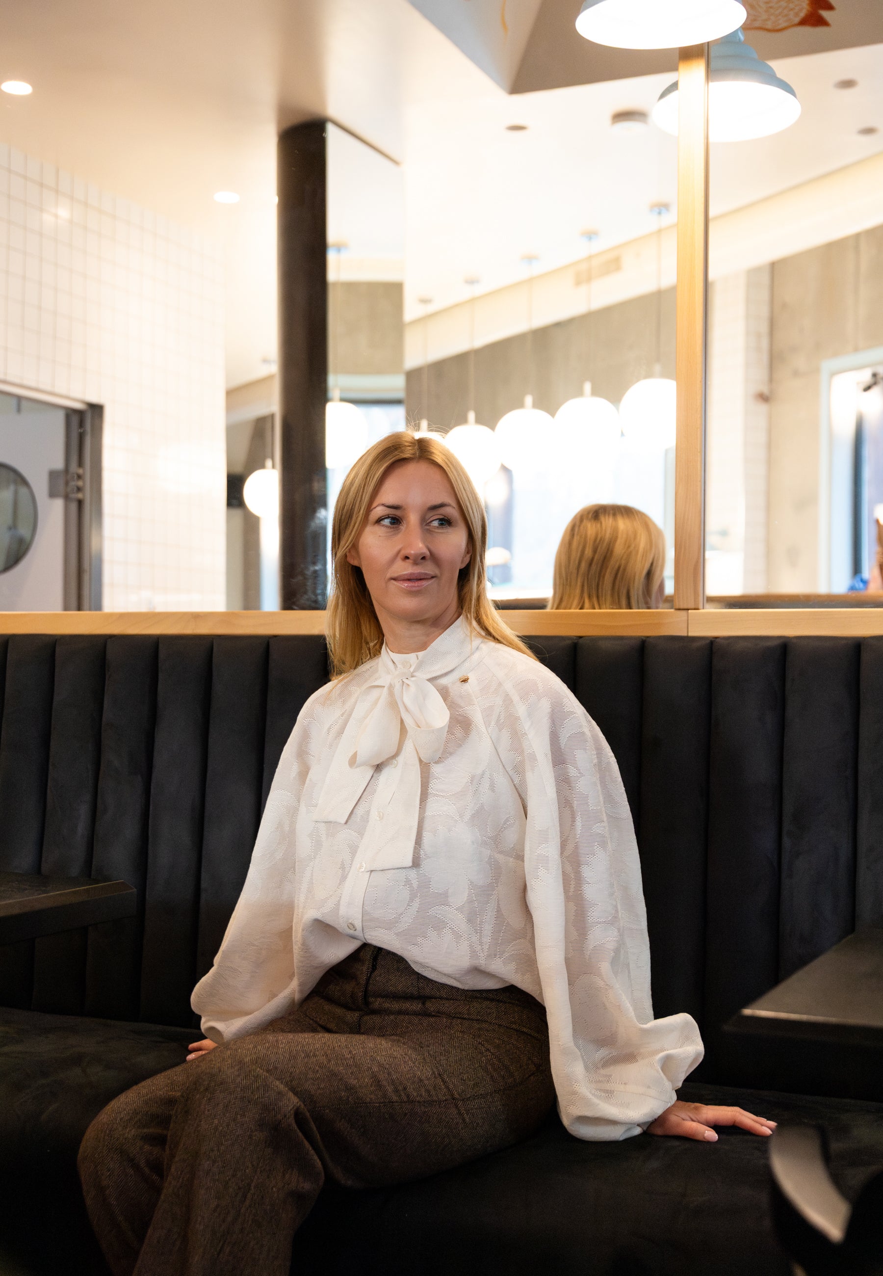 Modelka siedząca na kanapie w restauracji ubrana w kremową koszulkę VALEA w kwiatowy wzór.