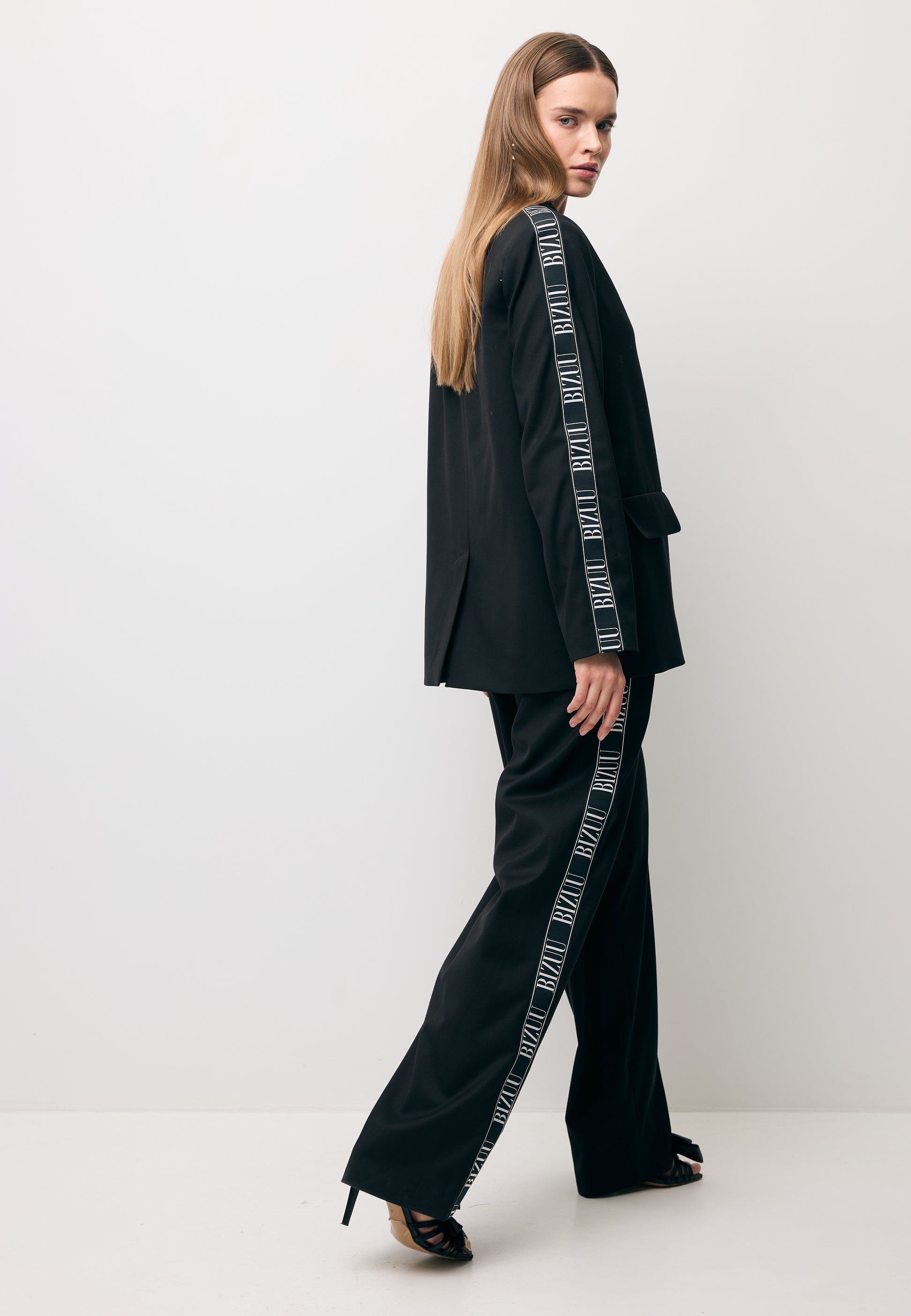 Modelka robiąca krok w bok w czarnym garniturze - oversizowa marynarka z lampasem VANDA oraz szerokie spodnie MICHAEL.