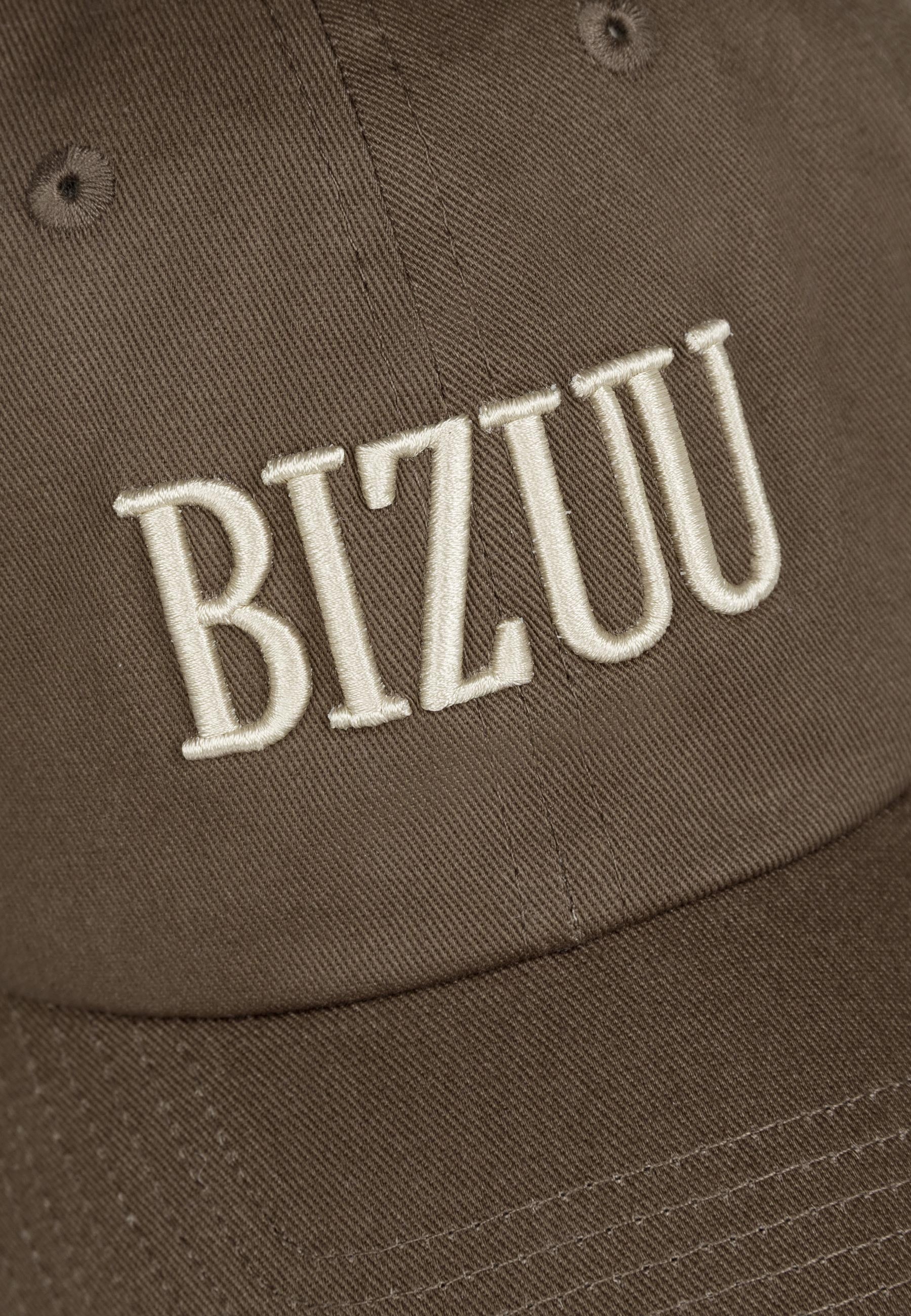 Zbliżenie na logo haftowane na przodzie czapki z daszkiem ZANE w kolorze brązowym.