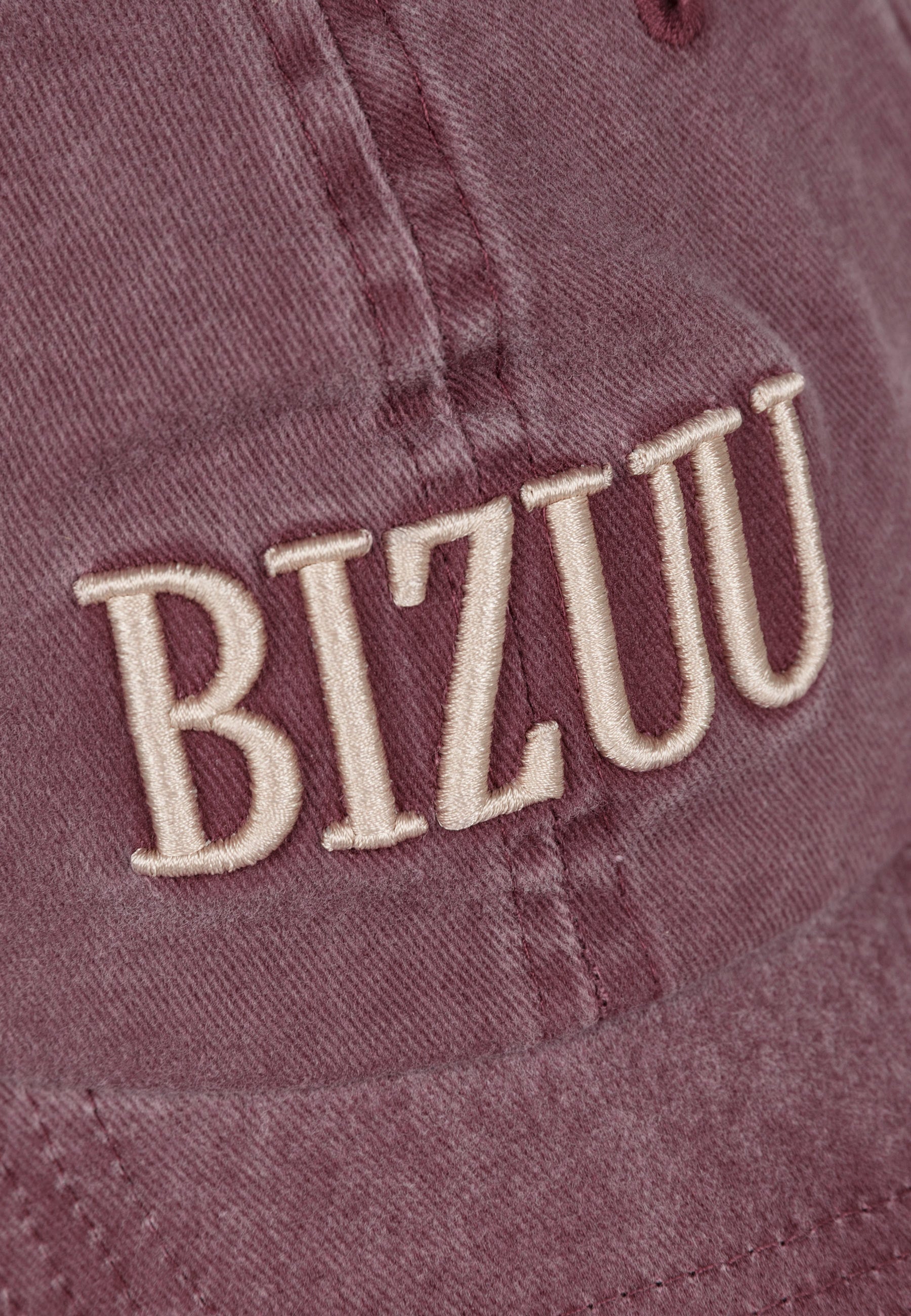 Zbliżenie na haftowane logo na przodzie bordowej czapki z daszkiem ZANE.