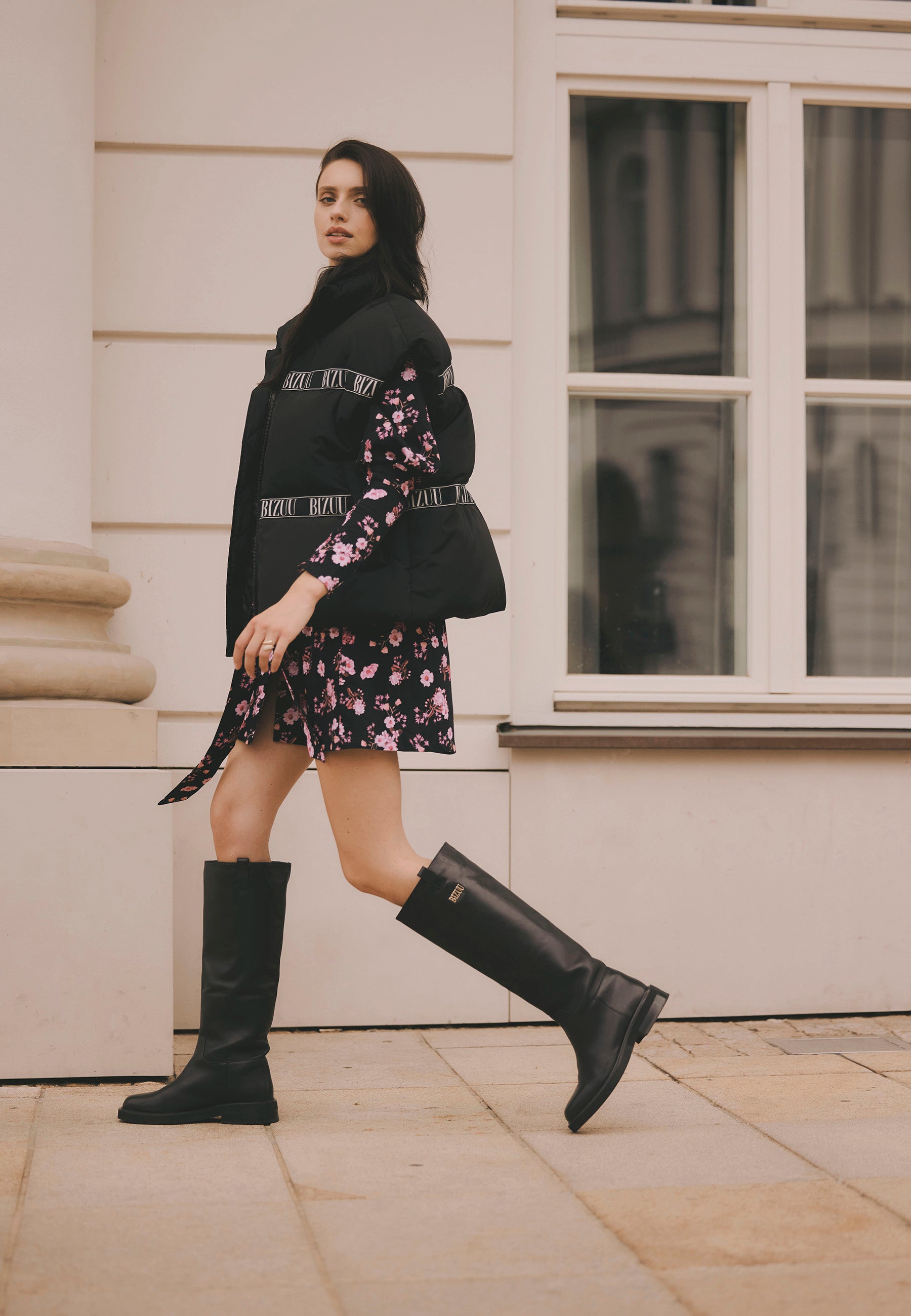Modelka idąca ulicą ubrana w kamizelkę z naturalnym wypełnieniem AYASE. sukienkę GEORGINA oraz skórzane kozaki CALYX.
